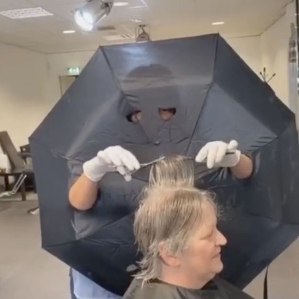 Hairdresser cuts holes in umbrella for arms and eyes as barrier between clients