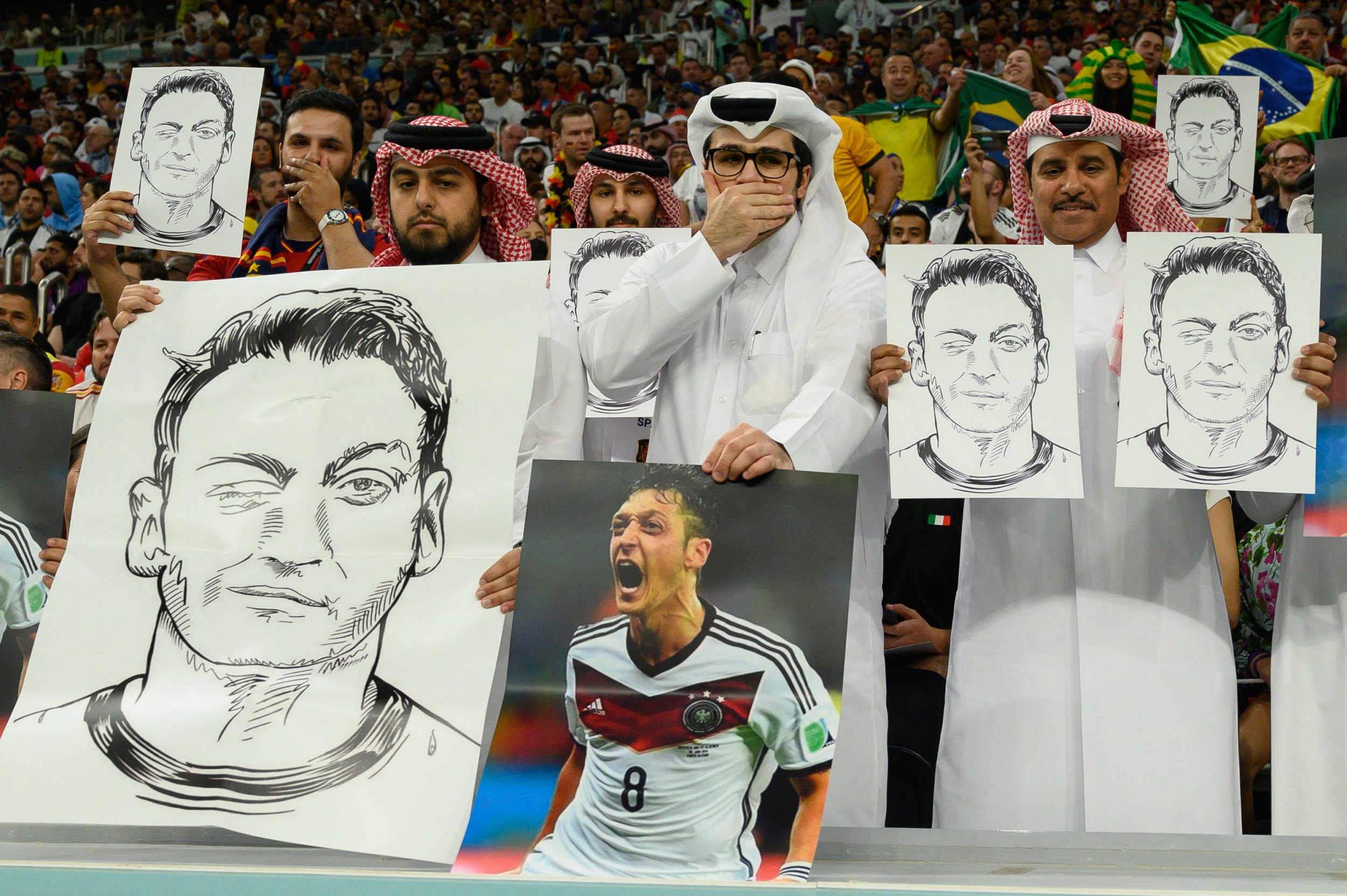 Qatari fans hold up pictures of Mesut Ozil to Germany supporters during World Cup game vs Spain